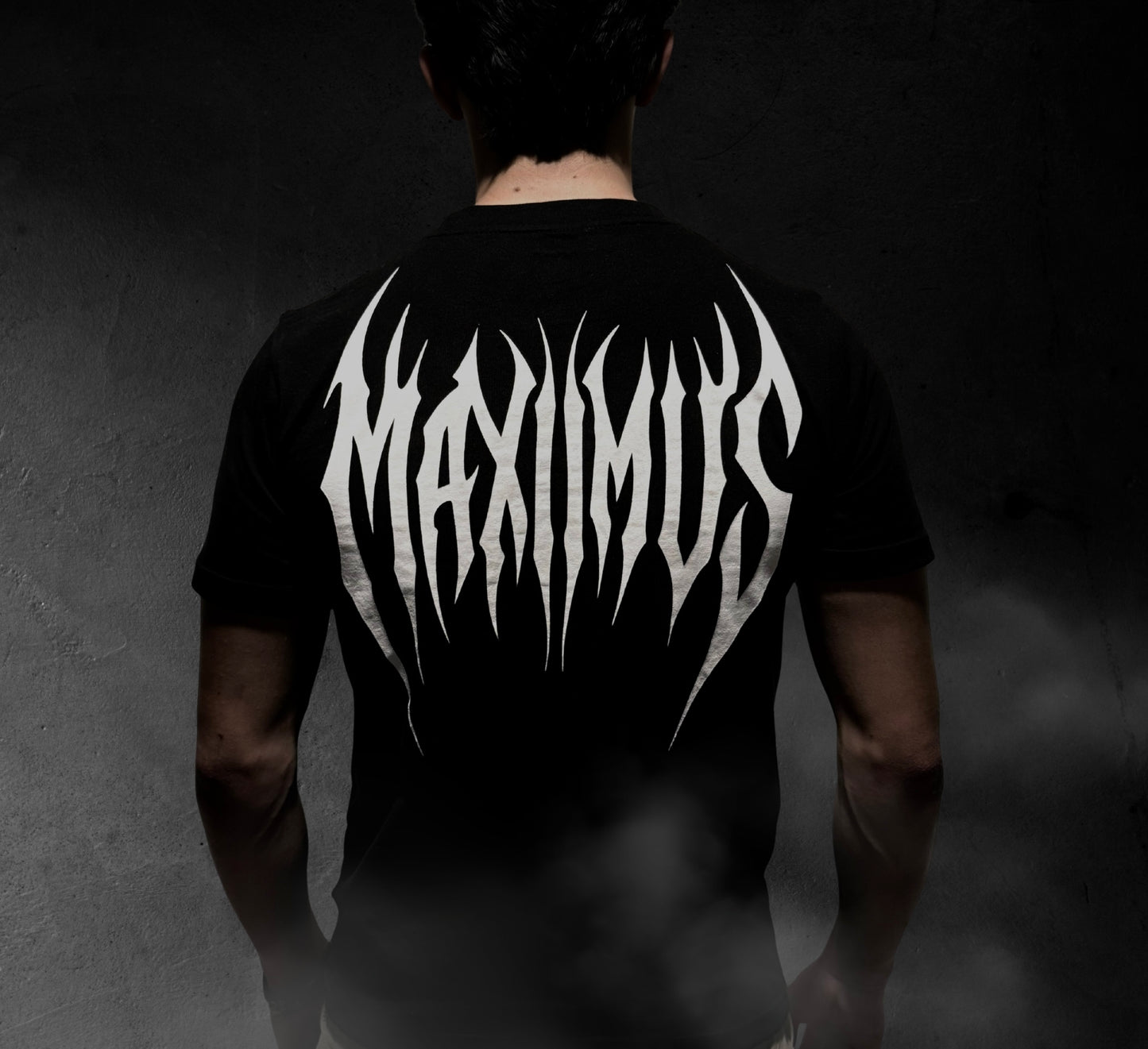 Person wearing a black t-shirt with 'MAXIMUS' design on the back against a dark background